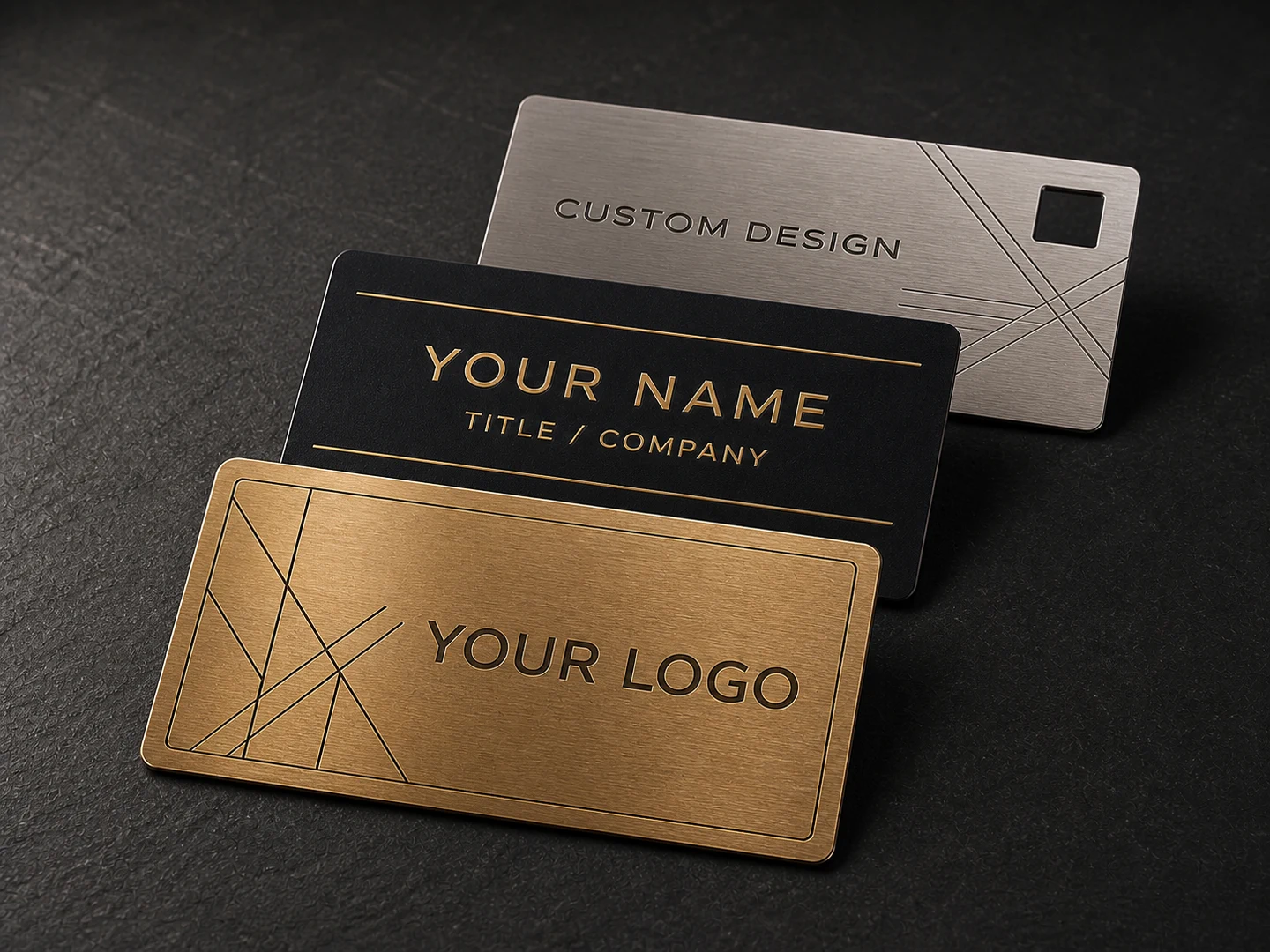 Three customizable metal business cards in gold, black and silver with etched text, linework and a geometric cutout.