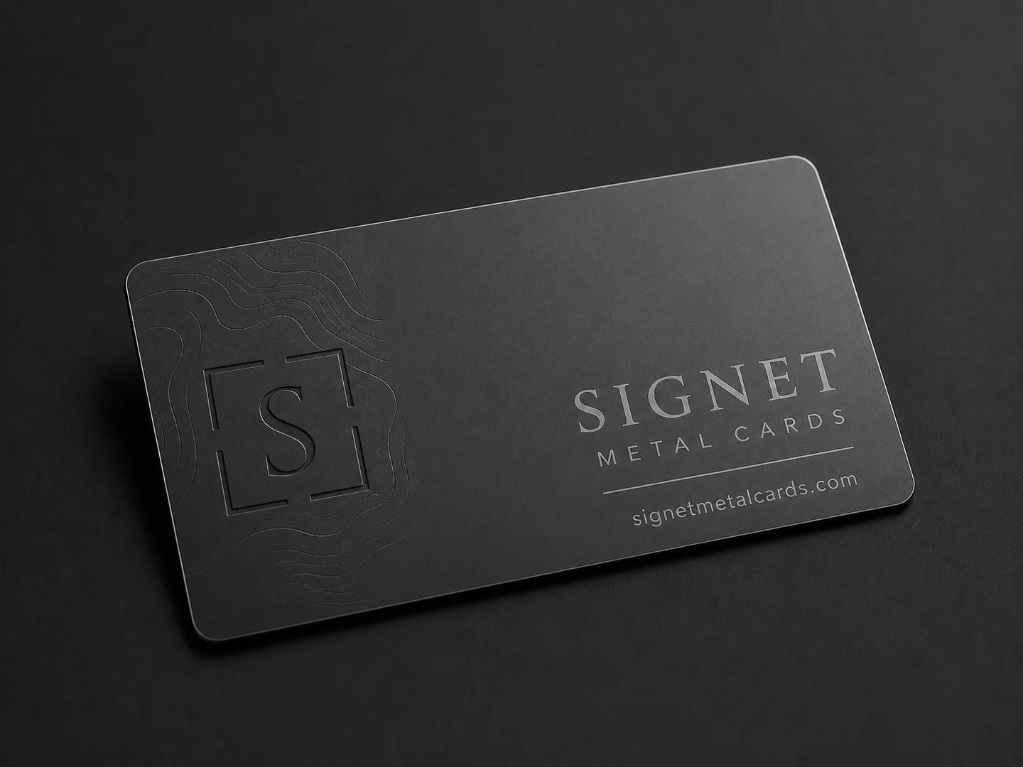 Dark etched metal business card with a recessed S monogram and Signet design